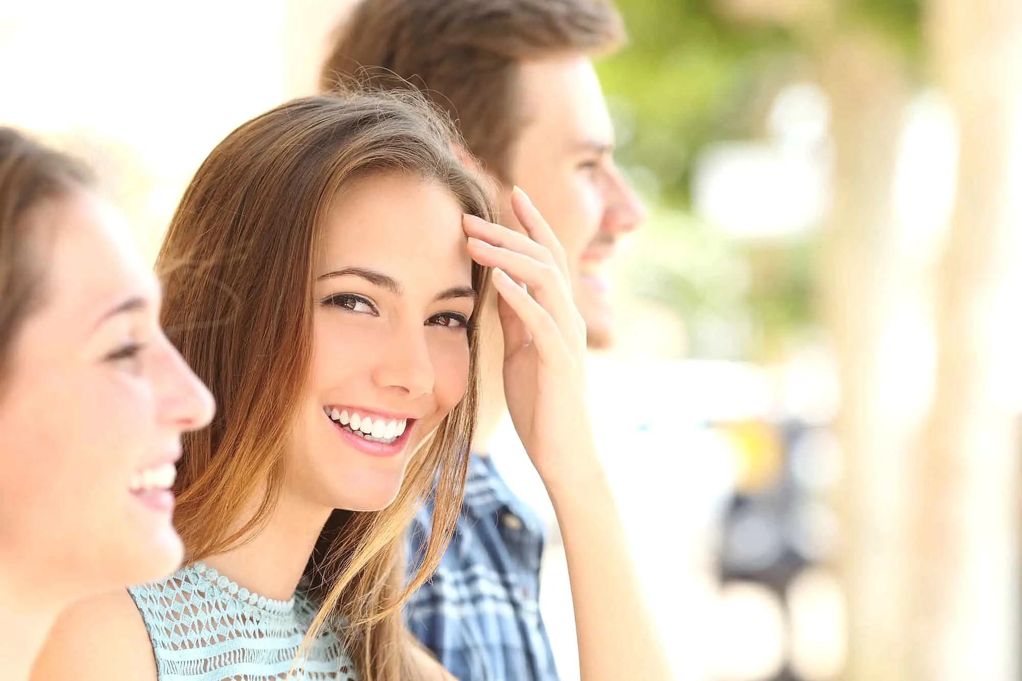 Three young adults enjoy a sunny day near Herbst Appliance, with the woman in front smiling at the camera while two friends beside her look away and smile. This cheerful scene captures the spirit of Smile City Orthodontics in Sunnyvale, TX.