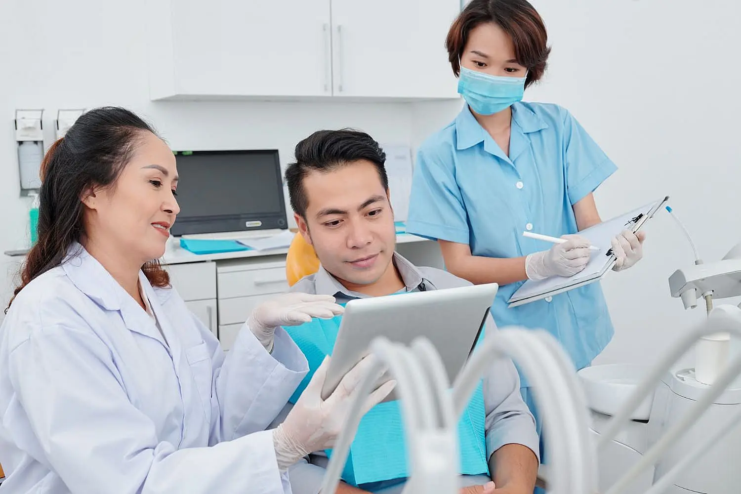 At Smile City Orthodontics in Sunnyvale TX, a dentist explains jaw surgery to a male patient using a tablet, while a dental assistant takes notes in the clinic.