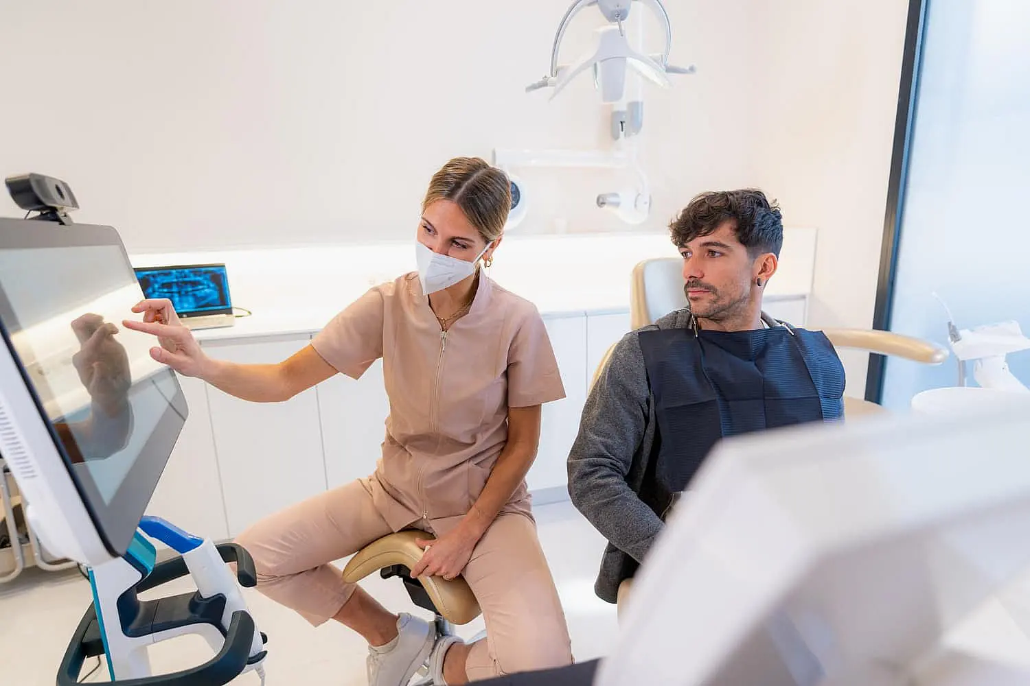 At Smile City Orthodontics in Sunnyvale TX, a dental professional explains tongue thrust to a seated patient while pointing at a monitor in the modern clinic.
