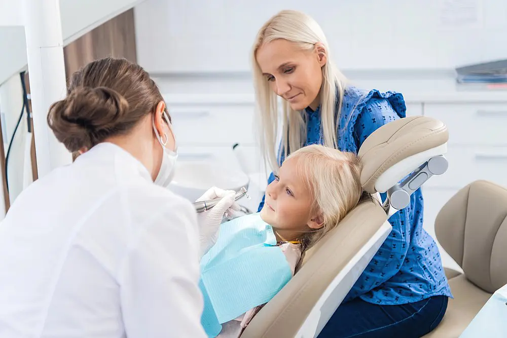 At Smile City Orthodontics in Sunnyvale TX, a children's orthodontist examines a young girl's teeth as her mother sits nearby in the inviting clinic.