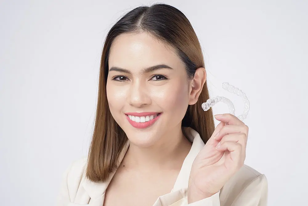 Woman smiling and holding a clear aligner tray for Smile City Orthodontics in Sunnyvale TX, with mention of Invisalign insurance.