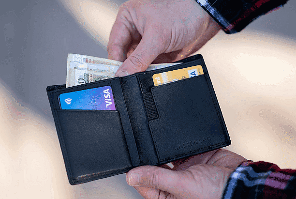 A person holds an open black wallet with cash, a Visa debit card, and another card—possibly contemplating an Invisalign payment plan at Smile City Orthodontics in Sunnyvale, TX.