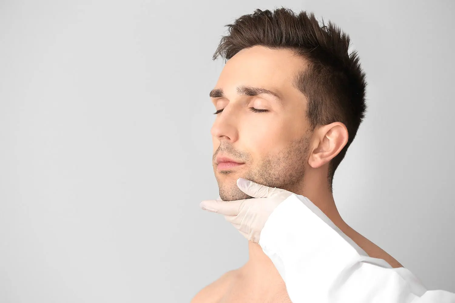 At Smile City Orthodontics in Sunnyvale TX, a gloved professional examines a person with closed eyes—possibly assessing them for jaw surgery—set against a plain light background.