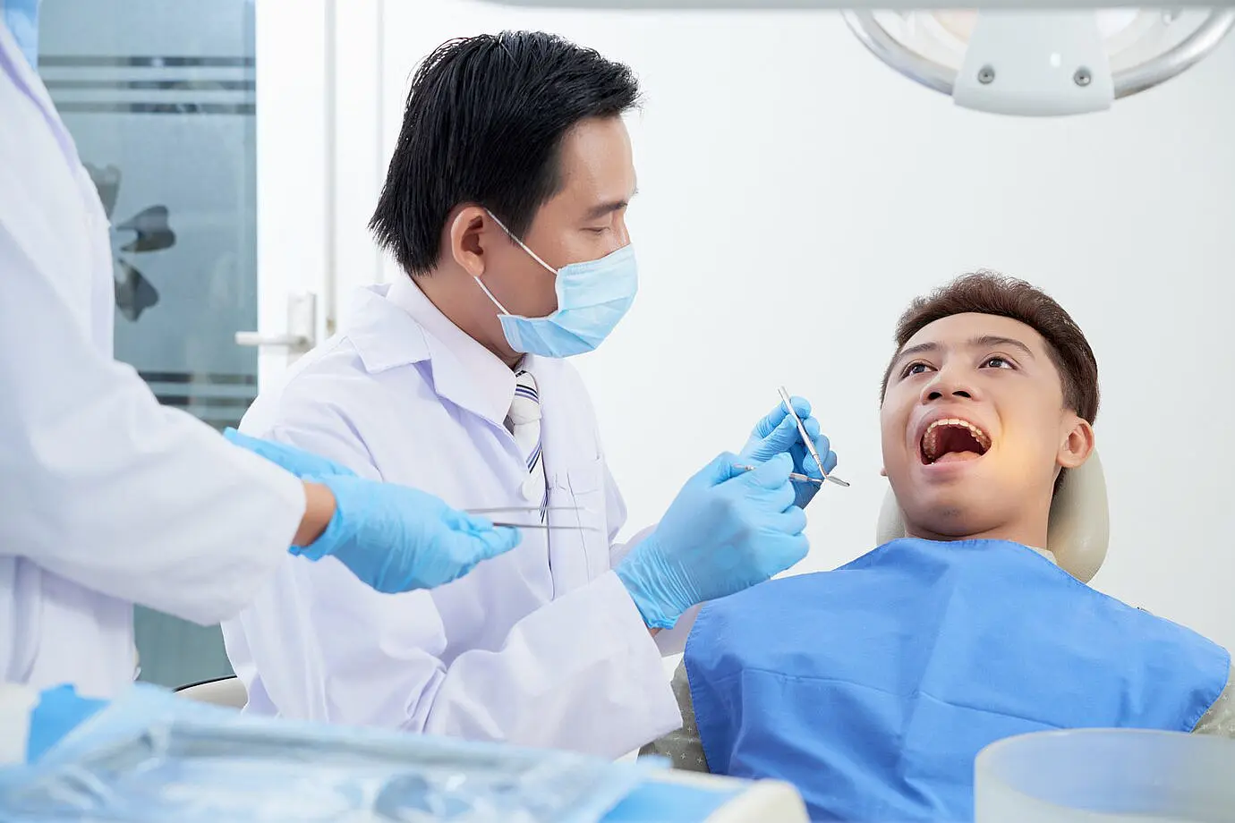 At Smile City Orthodontics in Sunnyvale TX, a masked dentist examines a patient's mouth for tongue thrust using dental tools, assisted by a nearby team member.