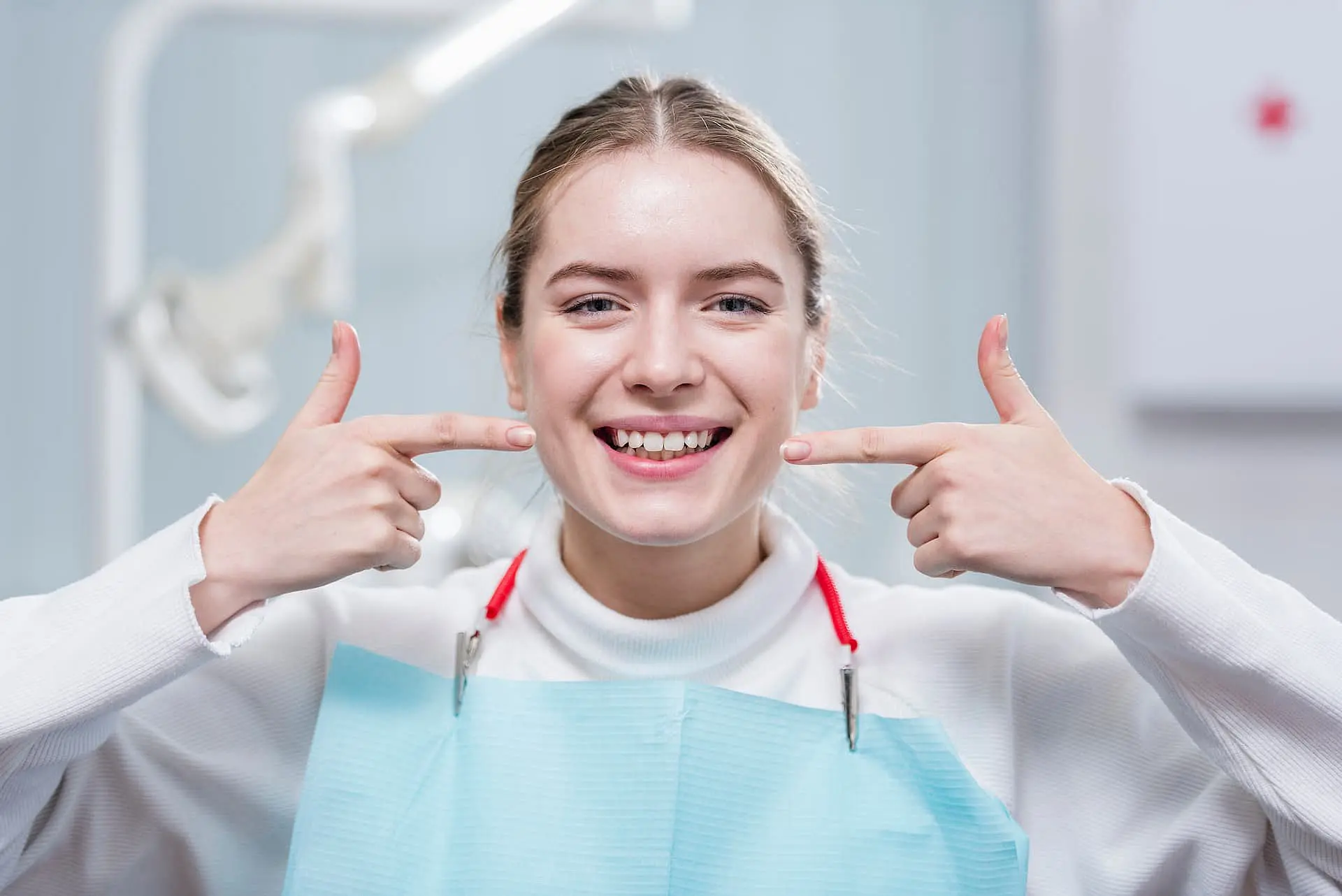 At Smile City Orthodontics in Sunnyvale TX, a young woman wearing a dental bib smiles and points to the gap between her upper front teeth to highlight her overbite.