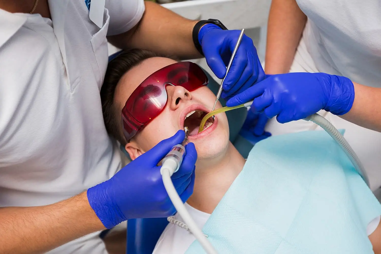 At Smile City Orthodontics in Sunnyvale TX, two professionals wearing gloves use dental instruments to treat a patient with Tongue Thrust, while the patient wears protective glasses.