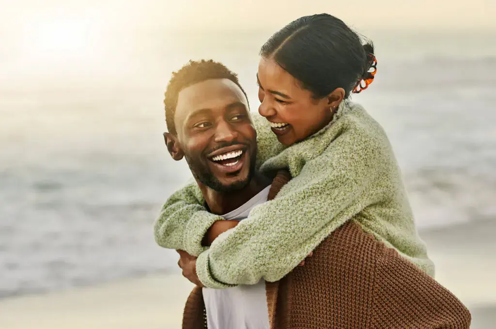 At the beach in Sunnyvale TX, a happy woman smiles while riding piggyback on a man, both in sweaters with the ocean behind them—a scene that captures the joy celebrated by Smile City Orthodontics. At the beach in Sunnyvale TX, a happy woman smiles while riding piggyback on a man, both in sweaters with the ocean behind them—a scene that captures the joy celebrated by Smile City Orthodontics.