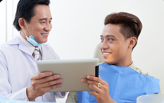 At Smile City Orthodontics in Sunnyvale TX, a dentist reviews jaw surgery details with a male patient, showing information on a tablet as the patient smiles in the dental chair.