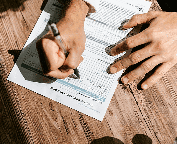 At Smile City Orthodontics in Sunnyvale TX, a person completes a consumer credit card application form on a wooden table, possibly thinking about expenses like Invisalign insurance.
