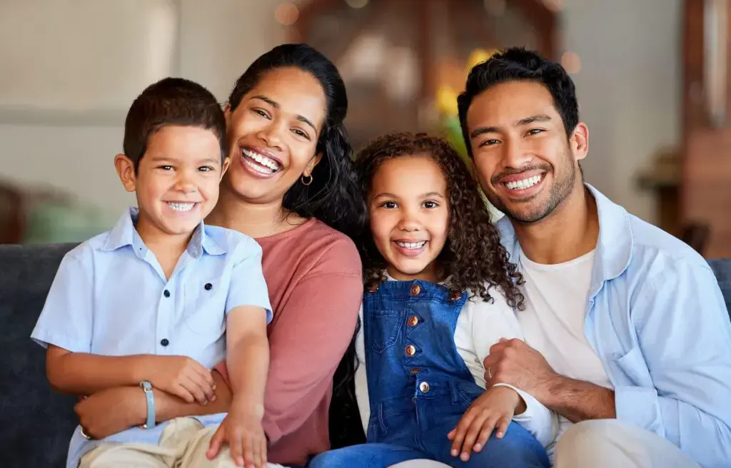 At Smile City Orthodontics in Sunnyvale TX, a family of four—two adults and two children—sits together on a well-lit couch, smiling at the camera. At Smile City Orthodontics in Sunnyvale TX, a family of four—two adults and two children—sits together on a well-lit couch, smiling at the camera.