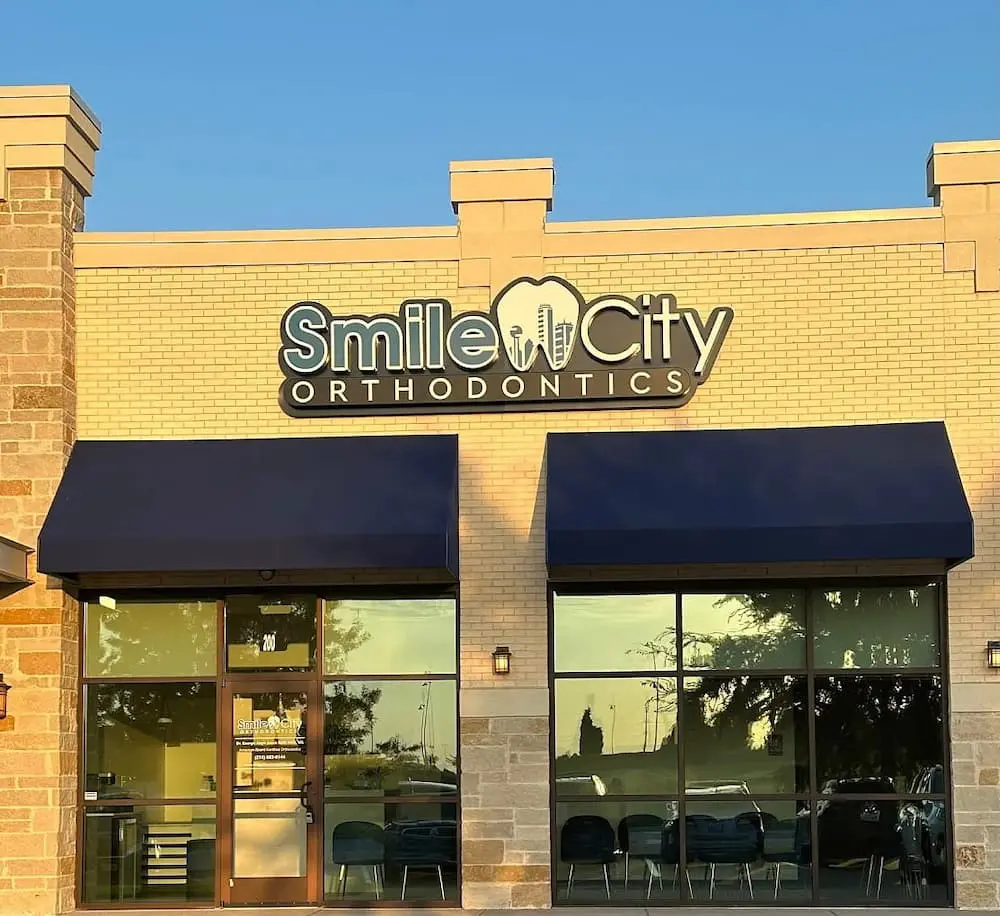The exterior of the Smile City Orthodontics office in Sunnyvale, TX features a prominent sign above the entrance and visible rows of chairs through the window.