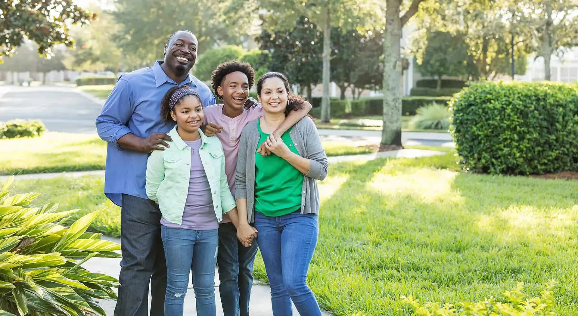 Enjoying peace of mind with their Orthodontic Insurance Plans, a family of four smiles for the camera on a sunny day surrounded by trees and lawn at Smile City Orthodontics in Sunnyvale, TX.