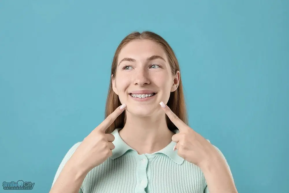 girl pointing her metal braces light blue background - How to Get Braces Glue Off Teeth in Sunnyvale, TX