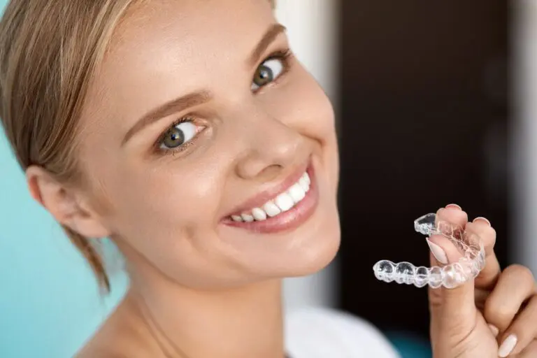 smiling woman with white teeth holding invisalign clear aligners - How Does Invisalign Work in Sunnyvale, TX?