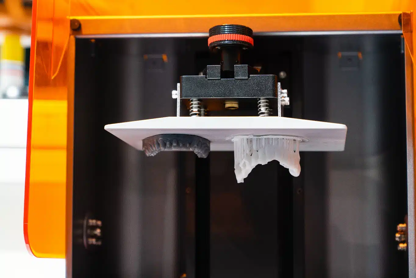 Inside Smile City Orthodontics in Sunnyvale, TX, a close-up of a resin 3D printer highlights advanced technology and two partially printed objects on its build platform.
