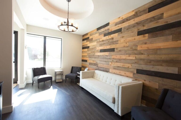 At Smile City Orthodontics in Sunnyvale TX, the modern waiting room features a white sofa, several black chairs, a wood-paneled accent wall, large windows, and a stylish ceiling light fixture.
