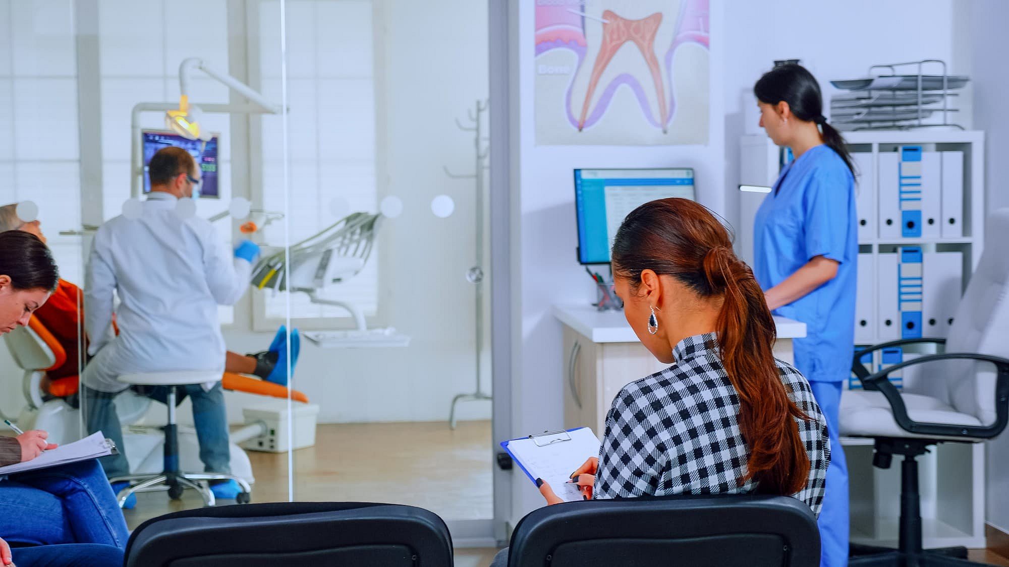 At Smile City Orthodontics in Sunnyvale TX, a woman completes paperwork—possibly reviewing orthodontic insurance plans—in the waiting area, as a dentist treats a patient behind glass and a nurse works at the computer.