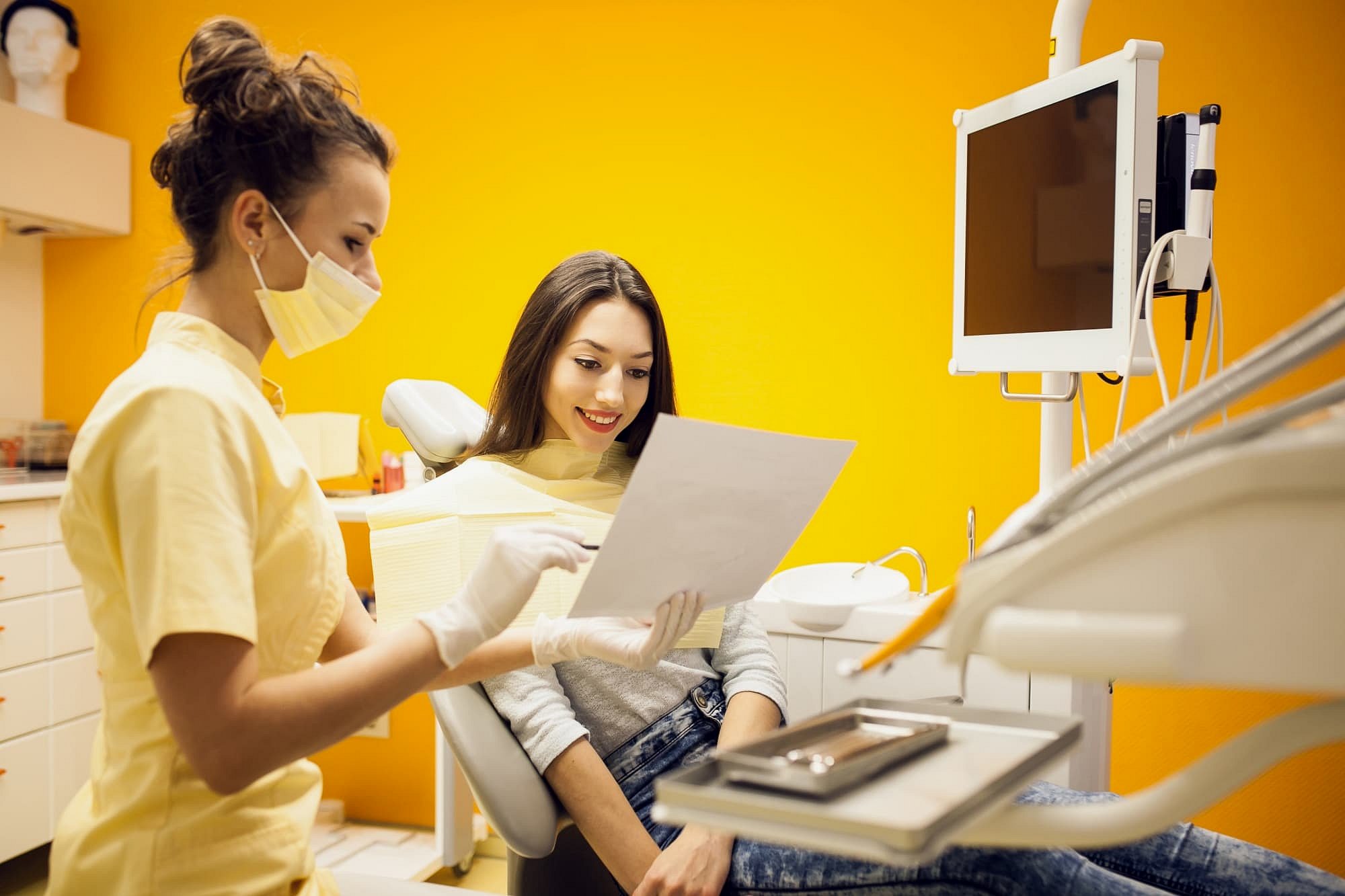 At Smile City Orthodontics in Sunnyvale TX, a dental professional explains orthodontic insurance plans to a smiling patient in an office featuring yellow walls and visible dental equipment.