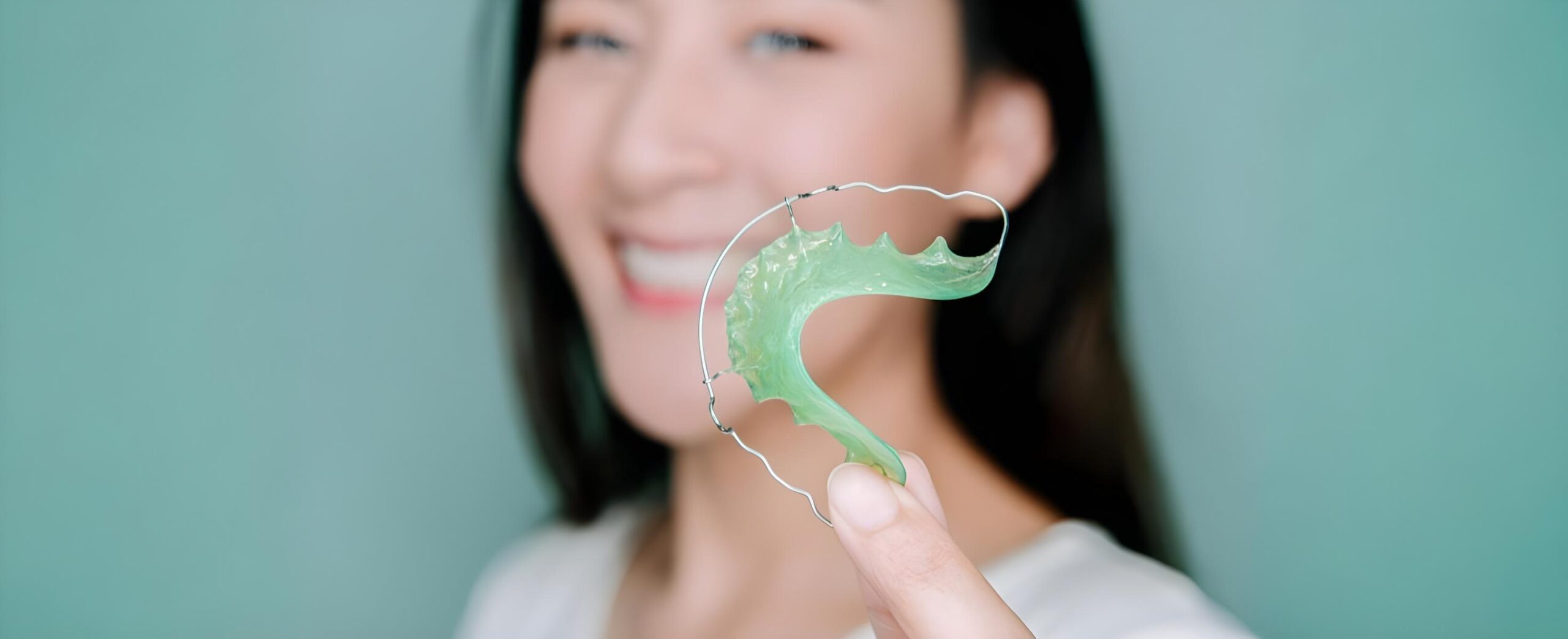 At Smile City Orthodontics in Sunnyvale, TX, a woman smiles while holding a green dental retainer in front of her face, showcasing how orthodontic appliances help maintain a beautiful smile.