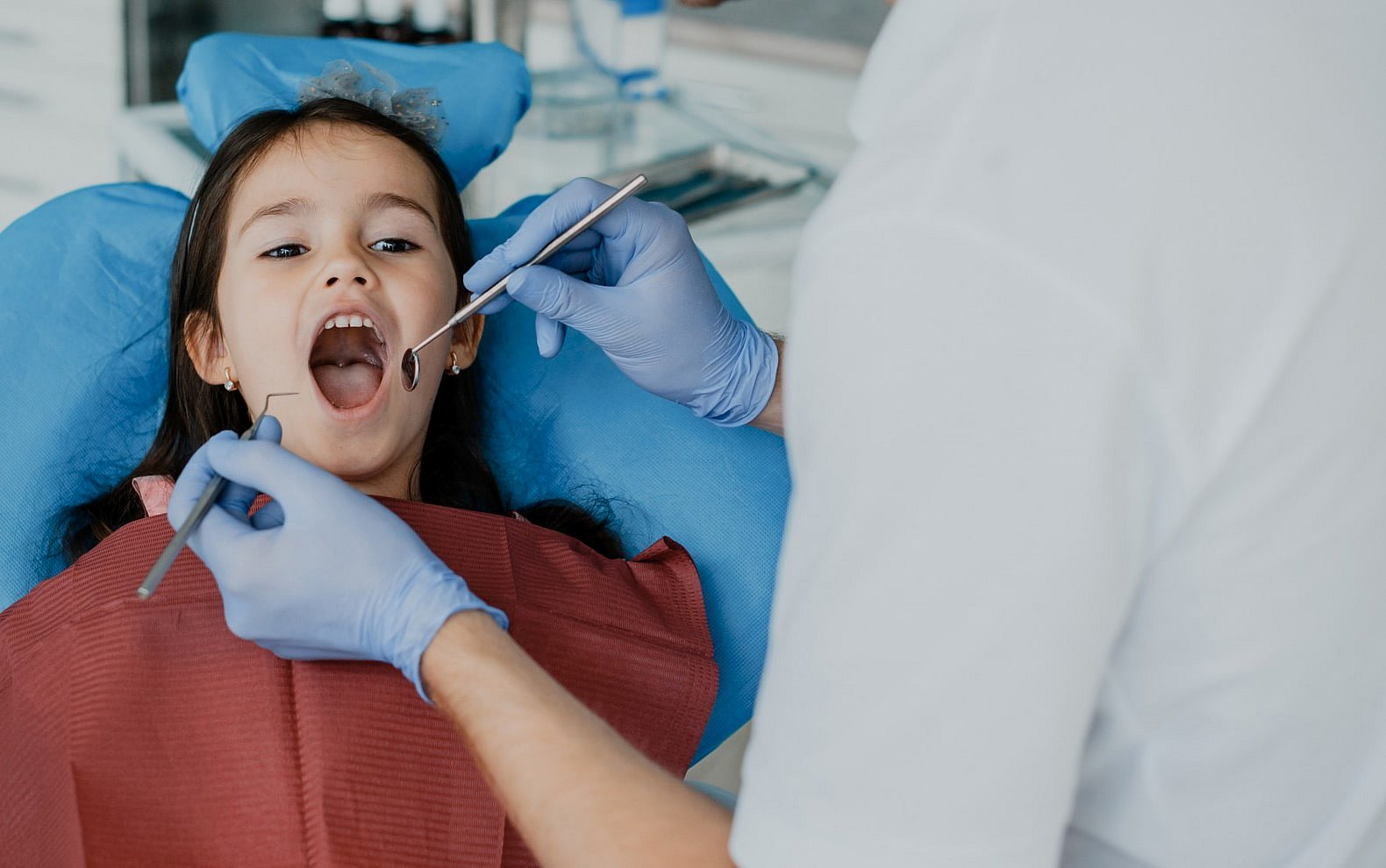 At Smile City Orthodontics in Sunnyvale TX, a children's orthodontist examines a young girl's teeth with dental instruments as she sits in the dental chair.