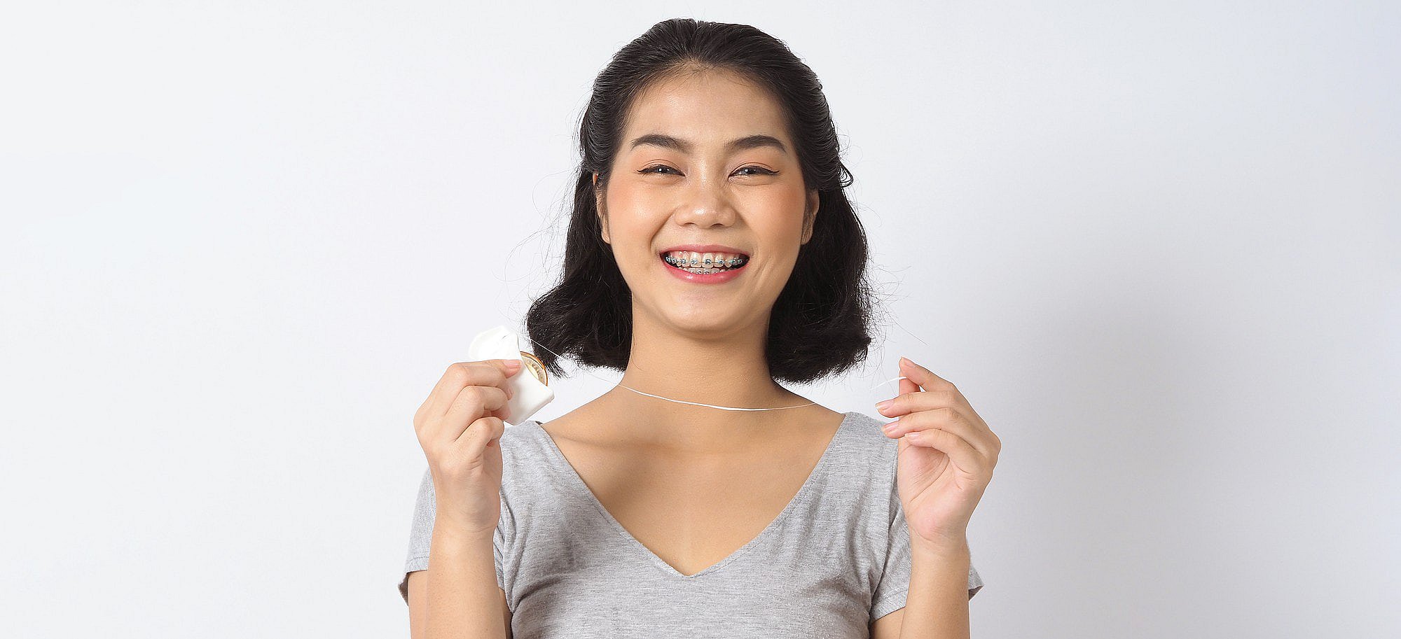 A woman with braces at Smile City Orthodontics in Sunnyvale, TX smiles as she holds dental floss, ready to carefully clean around her braces.