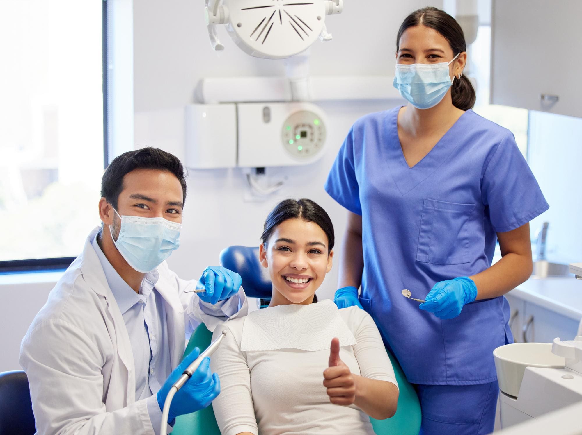 At Smile City Orthodontics in Sunnyvale TX, a patient with an underbite gives a thumbs up from the dental chair as two masked and gloved professionals smile beside her.