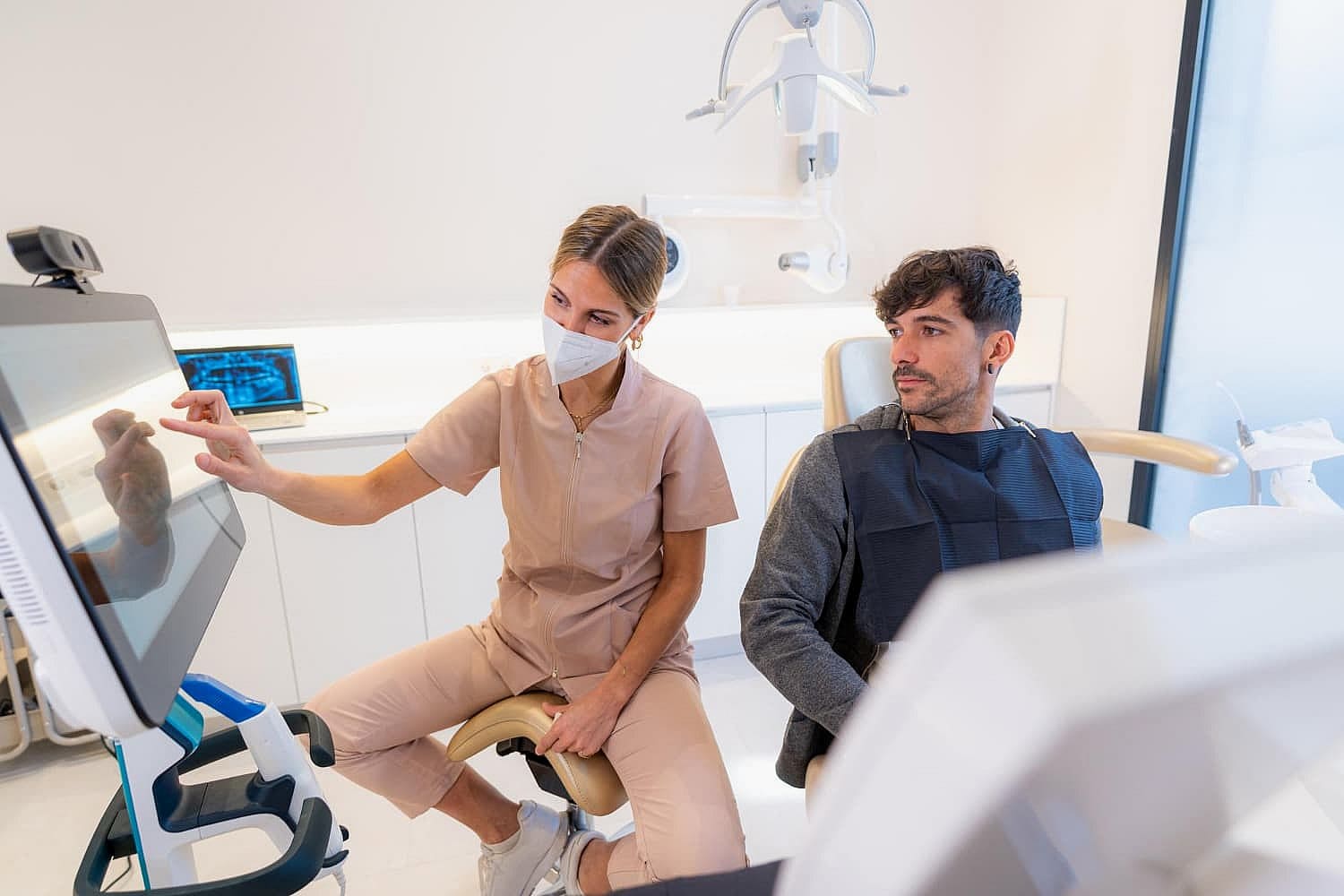 At Smile City Orthodontics in Sunnyvale TX, a dental professional explains tongue thrust to a seated patient while pointing at a monitor in the modern clinic.