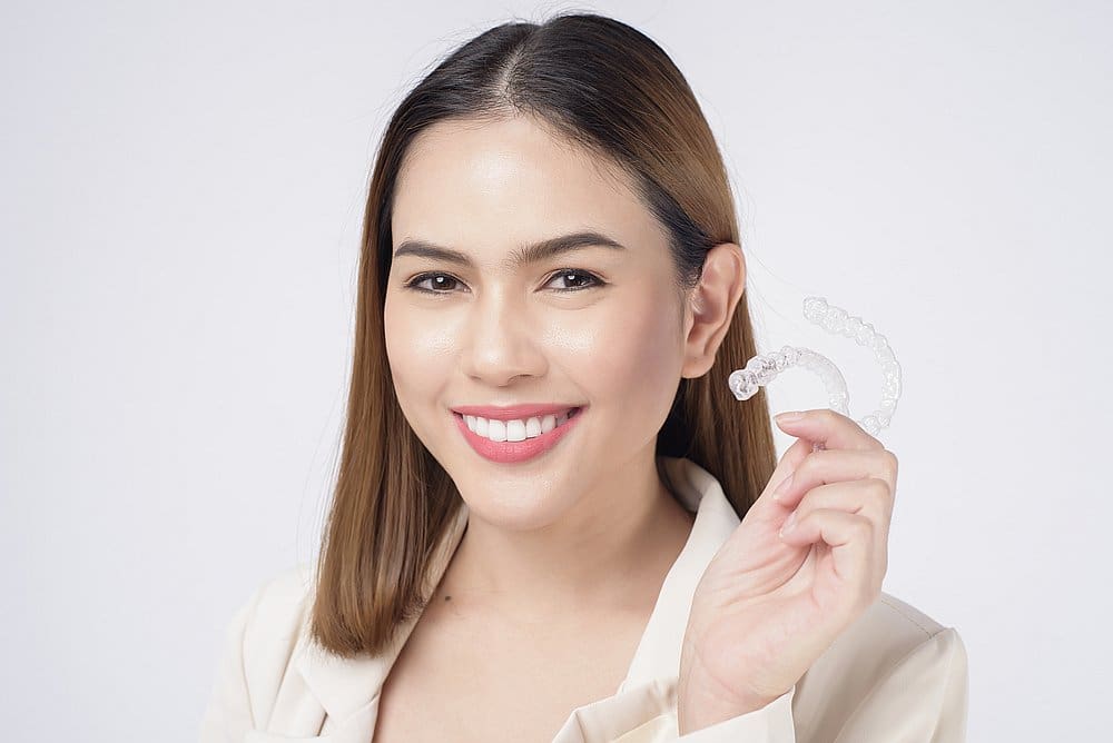 Woman smiling and holding a clear aligner tray for Smile City Orthodontics in Sunnyvale TX, with mention of Invisalign insurance.