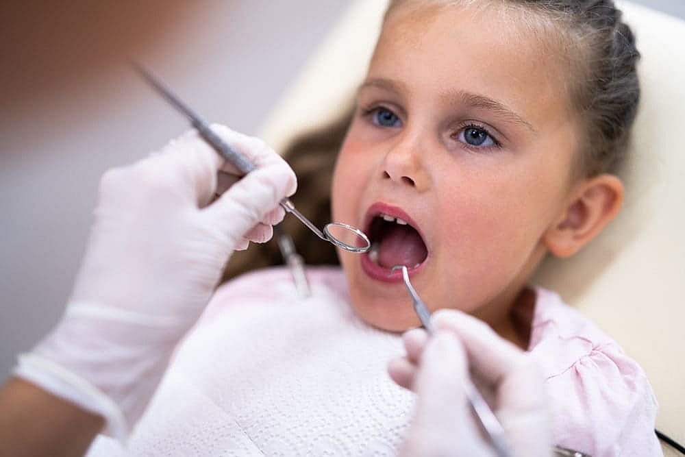 At Smile City Orthodontics in Sunnyvale TX, a dentist uses dental tools to check a young girl’s teeth for signs of tongue thrust as she sits in the chair.