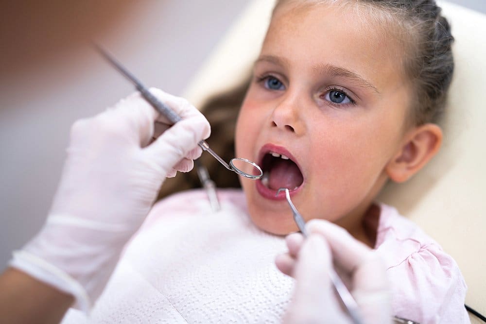 At Smile City Orthodontics in Sunnyvale TX, a children's orthodontist examines a young patient’s teeth while she sits in the dental chair.