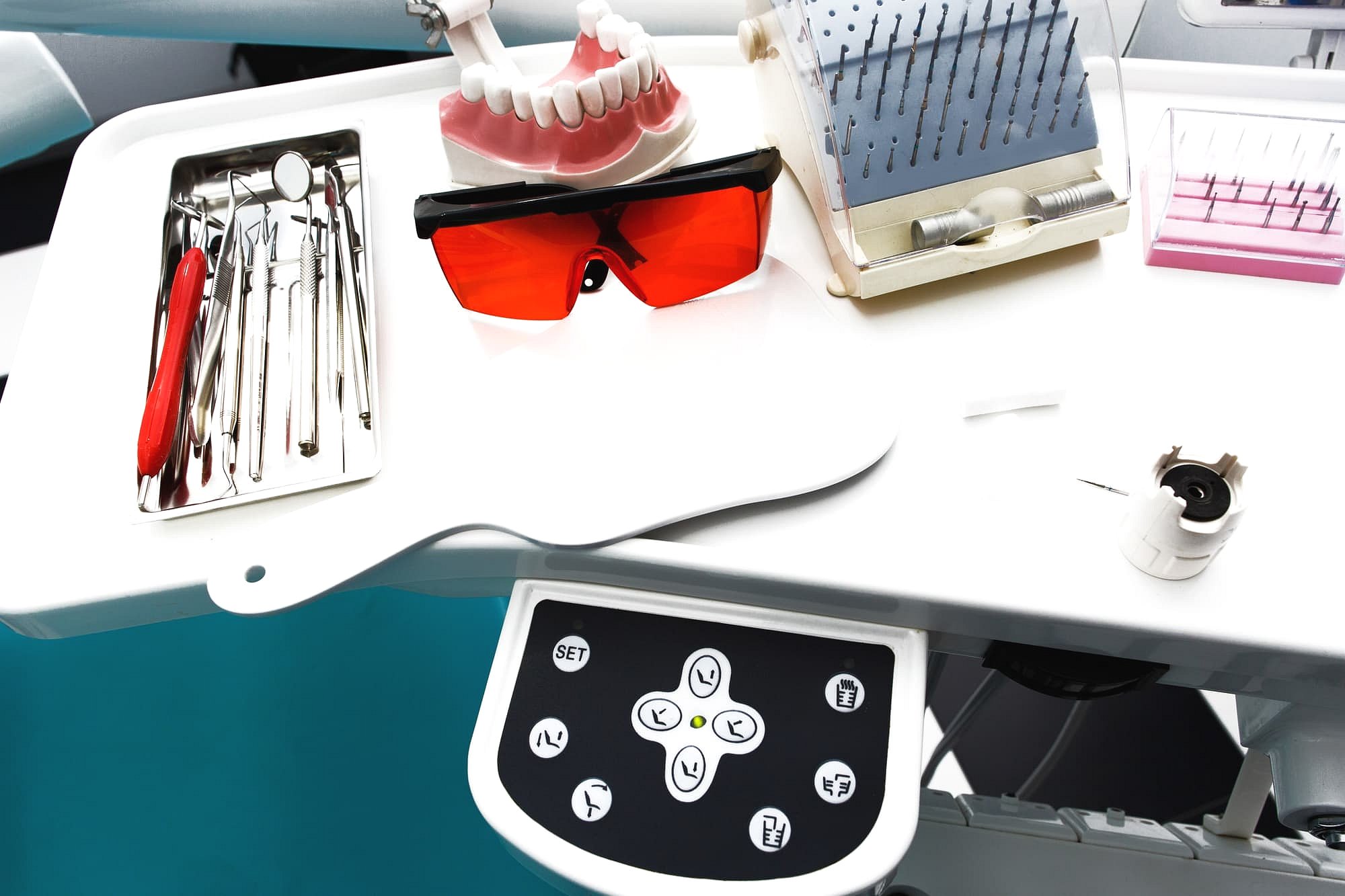 A dental tray at Smile City Orthodontics in Sunnyvale, TX displays metal braces tools, red protective glasses, a handheld mirror, and equipment controls on a white surface.