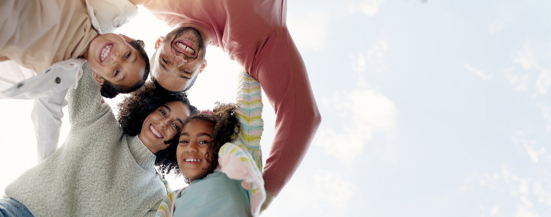 At Smile City Orthodontics in Sunnyvale TX, two adults and two children stand outdoors in a circle, smiling confidently with arms around each other. The adults’ smiles highlight the benefits of adult orthodontics against a clear sky backdrop.