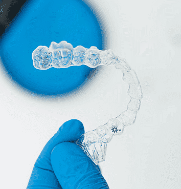 At Smile City Orthodontics in Sunnyvale TX, a gloved hand displays a clear dental aligner against a blue and white background, emphasizing options such as an Invisalign payment plan.