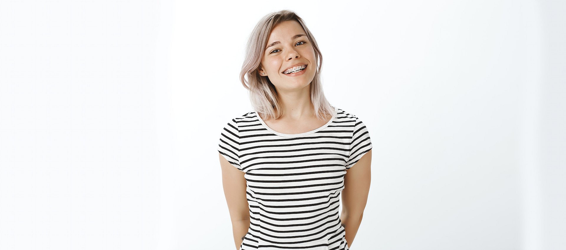At Smile City Orthodontics in Sunnyvale, TX, a young woman with light hair confidently smiles with her adult braces, wearing a black and white striped t-shirt against a plain white background.