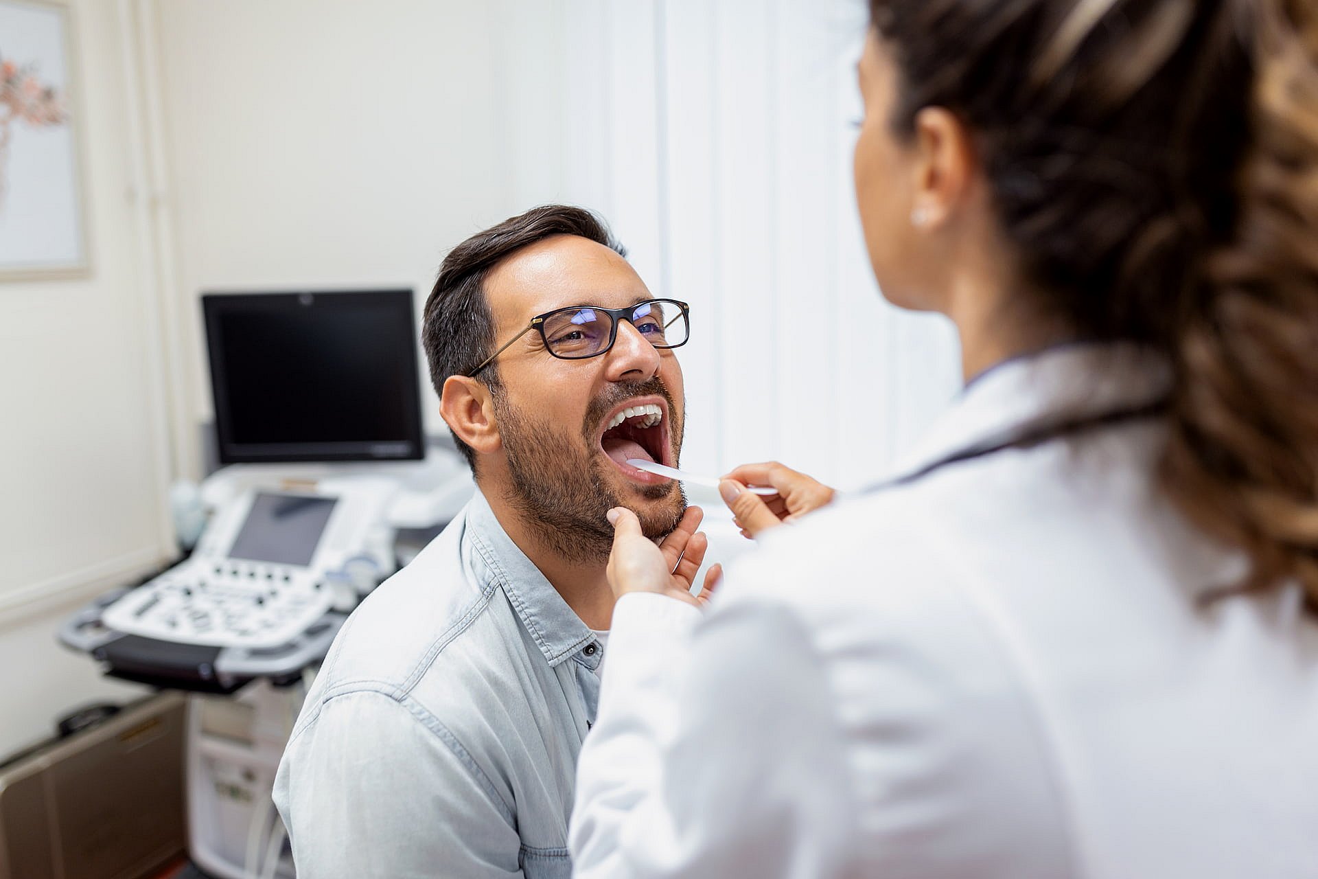 At Smile City Orthodontics in Sunnyvale TX, a doctor uses a tongue depressor to examine a male patient's throat for signs of tongue thrust.