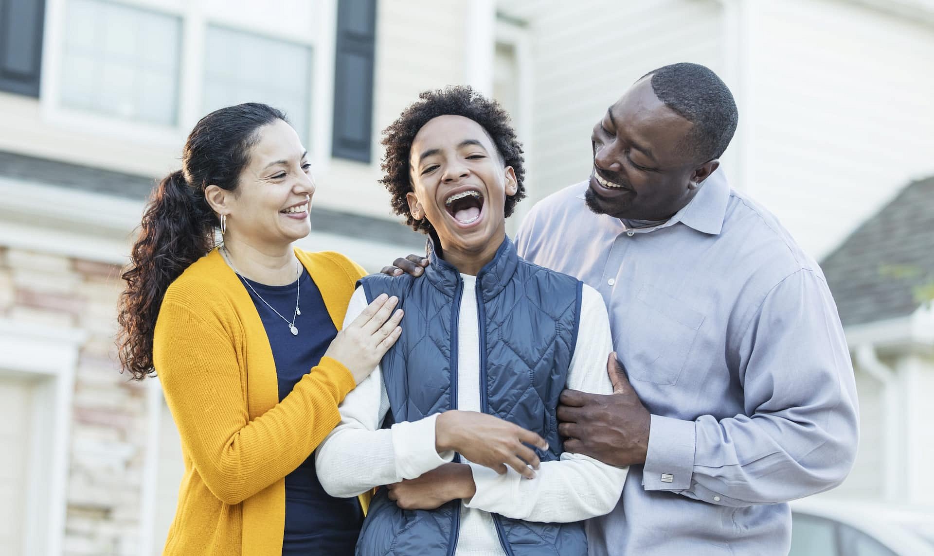 Outside a house in Sunnyvale TX, three people—including a teen and two adults dressed casually—share smiles and laughter, reflecting the friendly atmosphere at Smile City Orthodontics.
