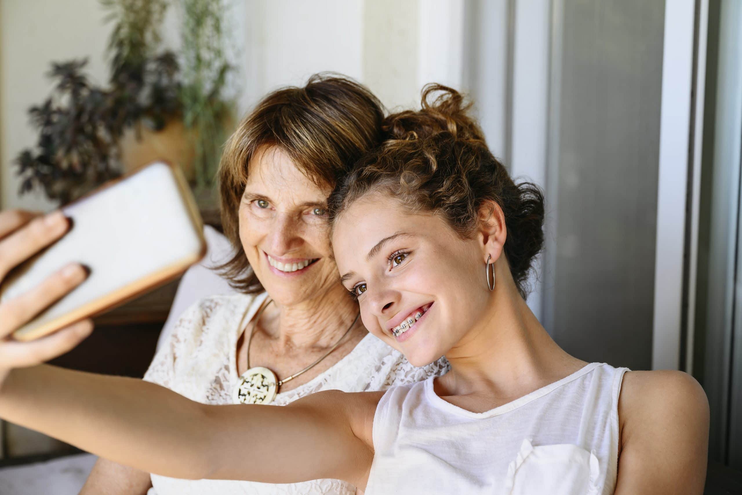 At Smile City Orthodontics in Sunnyvale TX, a young woman with braces takes a selfie with an older woman; both are smiling indoors, possibly discussing Invisalign cost for a brighter smile.