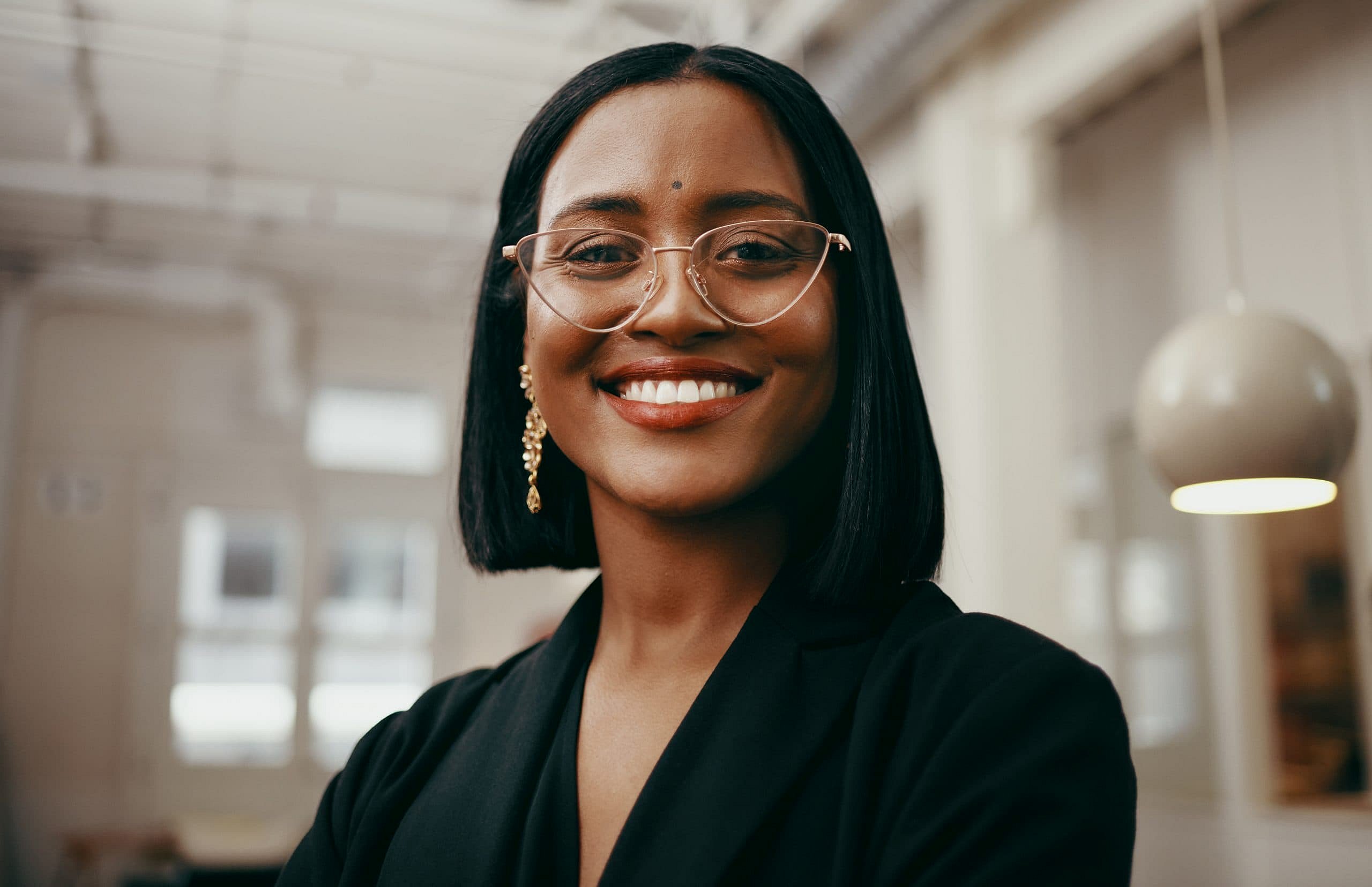 At Smile City Orthodontics in Sunnyvale TX, a confident woman with straight black hair, glasses, and a black blazer smiles in a modern office, prepared to discuss Orthodontic Insurance Plans.