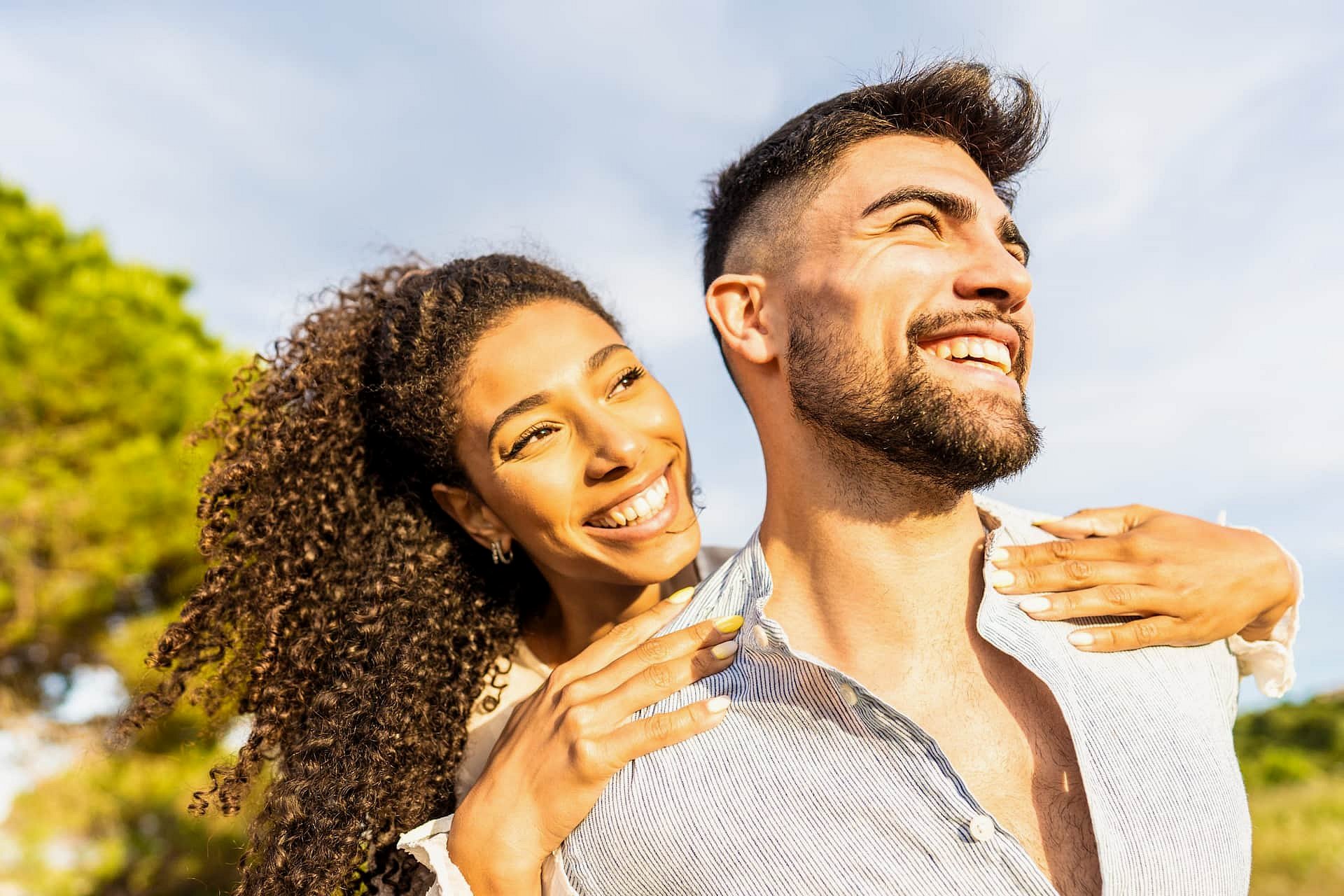 A woman gives a piggyback ride to a smiling man outdoors on a sunny day, both radiating confidence after treatment at Smile City Orthodontics in Sunnyvale, TX.