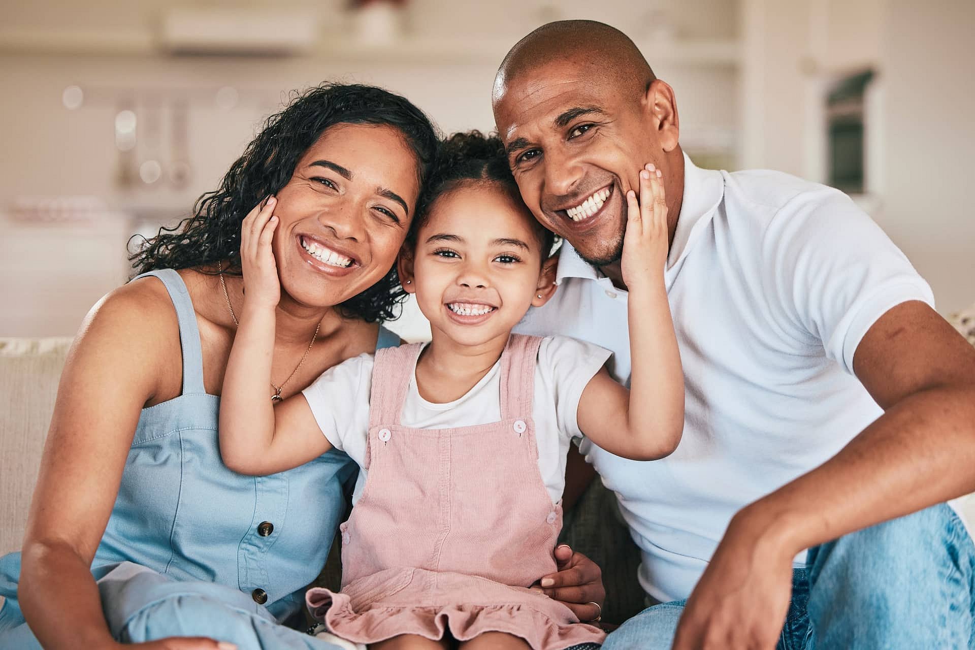 At Smile City Orthodontics in Sunnyvale TX, a smiling man, woman, and young girl with a palatal expander sit closely on a couch as the child places her hands on their faces.