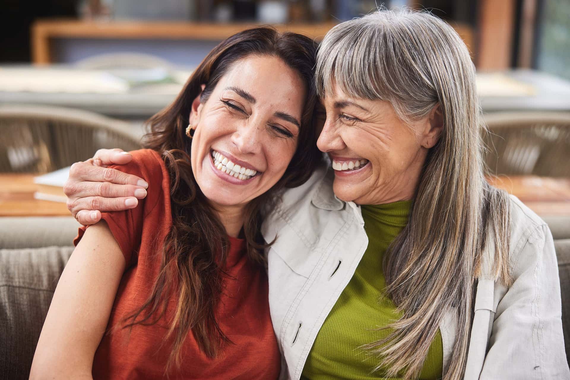 At Smile City Orthodontics in Sunnyvale TX, two women sit close together on a couch, smiling and laughing with confidence after getting affordable Invisalign.