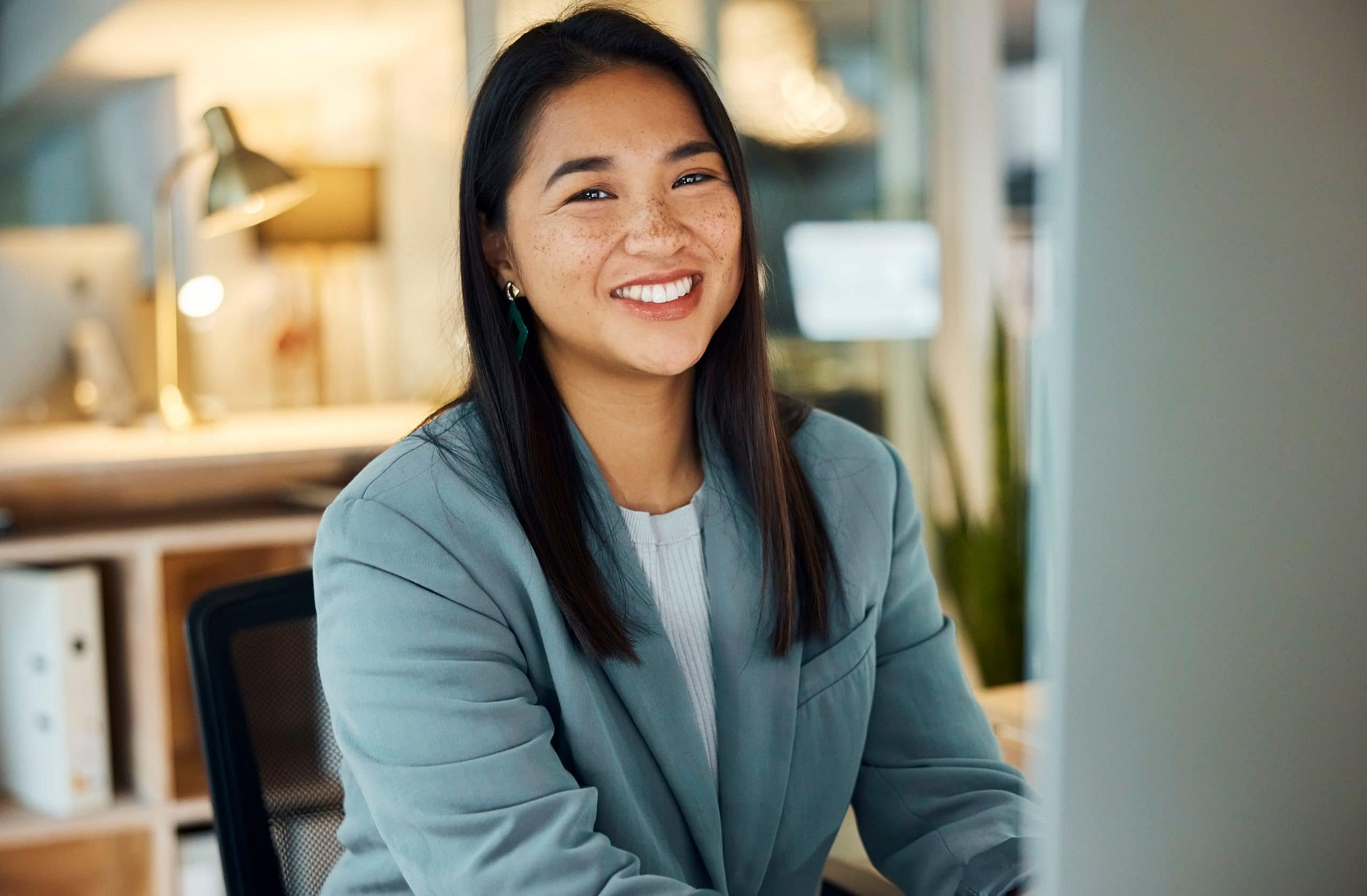 At Smile City Orthodontics in Sunnyvale TX, a woman in a blue blazer sits at a modern office desk, smiling and ready to discuss your Braces Payment Plan options.