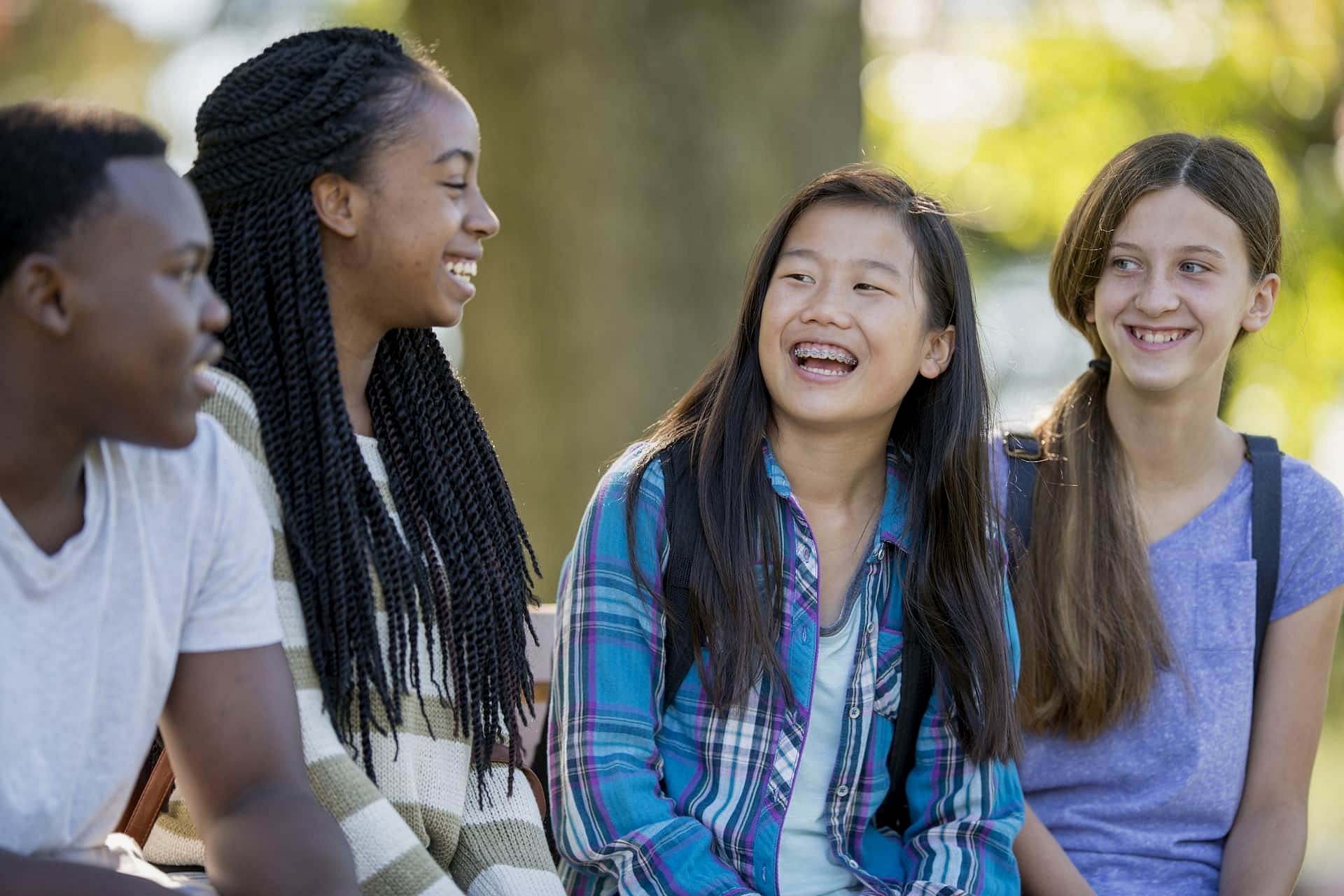 A group of four teenagers sits on a bench, smiling and chatting in a park, possibly discussing how an Invisalign Payment Plan from Smile City Orthodontics in Sunnyvale TX, can help them achieve confident smiles.