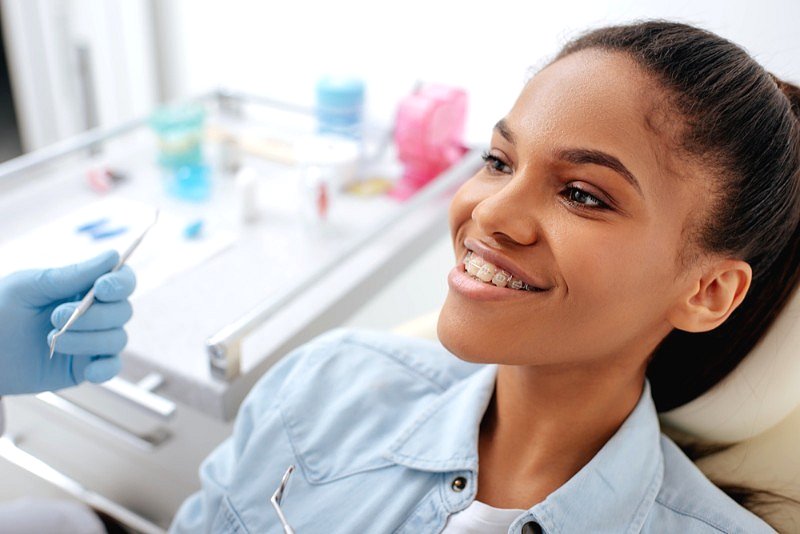 At Smile City Orthodontics in Sunnyvale TX, a young person with clear ceramic braces smiles in the dental chair as a gloved professional prepares an instrument.