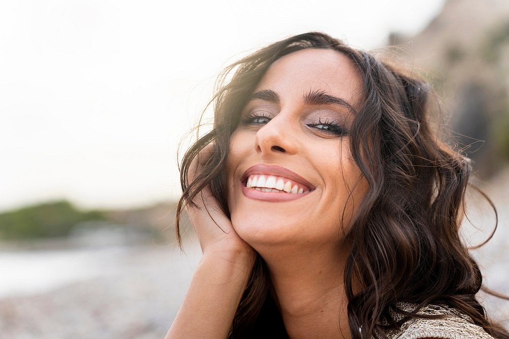 At Smile City Orthodontics in Sunnyvale TX, a woman with long brown hair smiles confidently at the camera outdoors, showcasing her transformation after jaw surgery against a blurred natural backdrop.