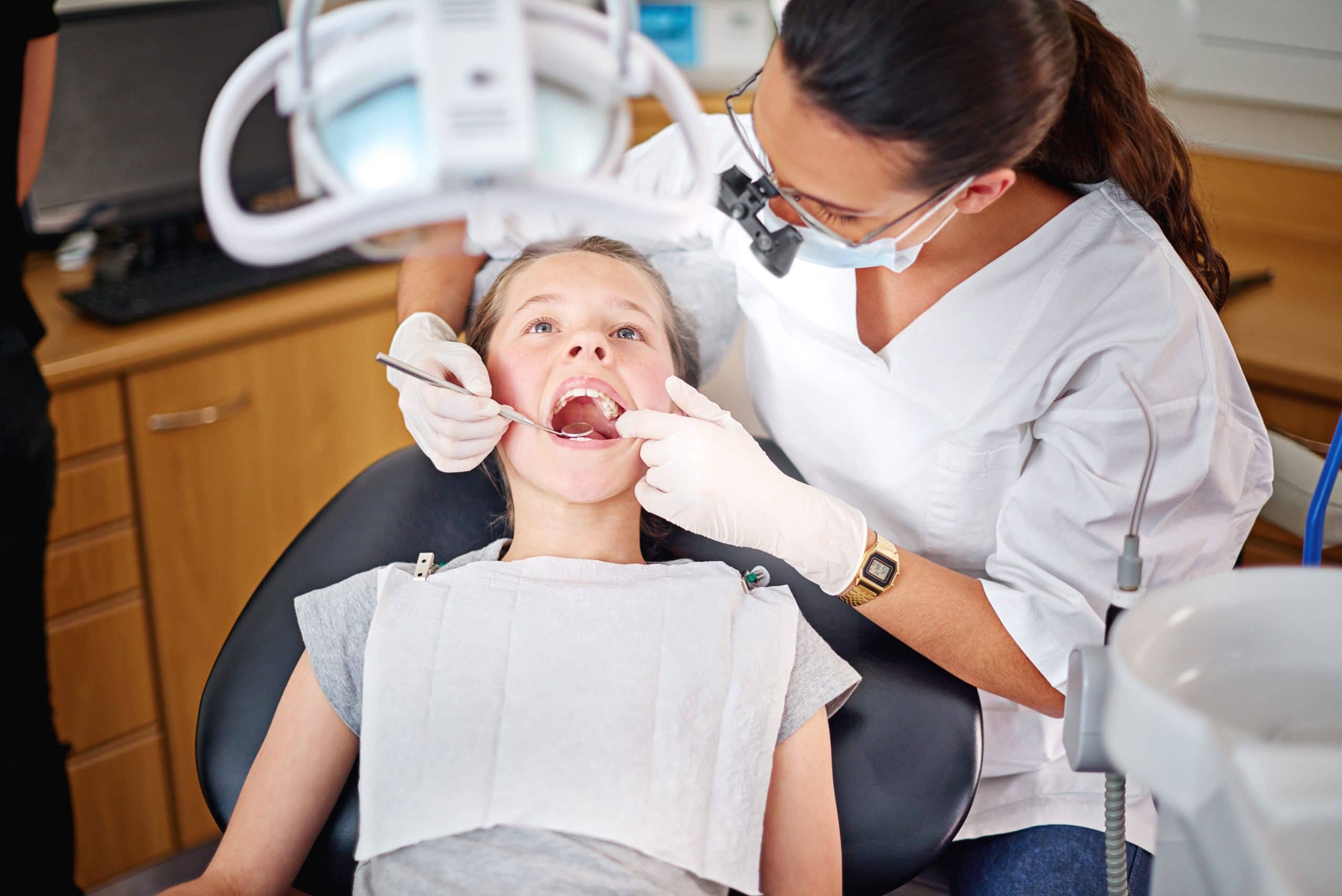 At Smile City Orthodontics in Sunnyvale TX, a dentist in a white coat examines a young patient's teeth and discusses Invisalign cost options in a modern clinic.