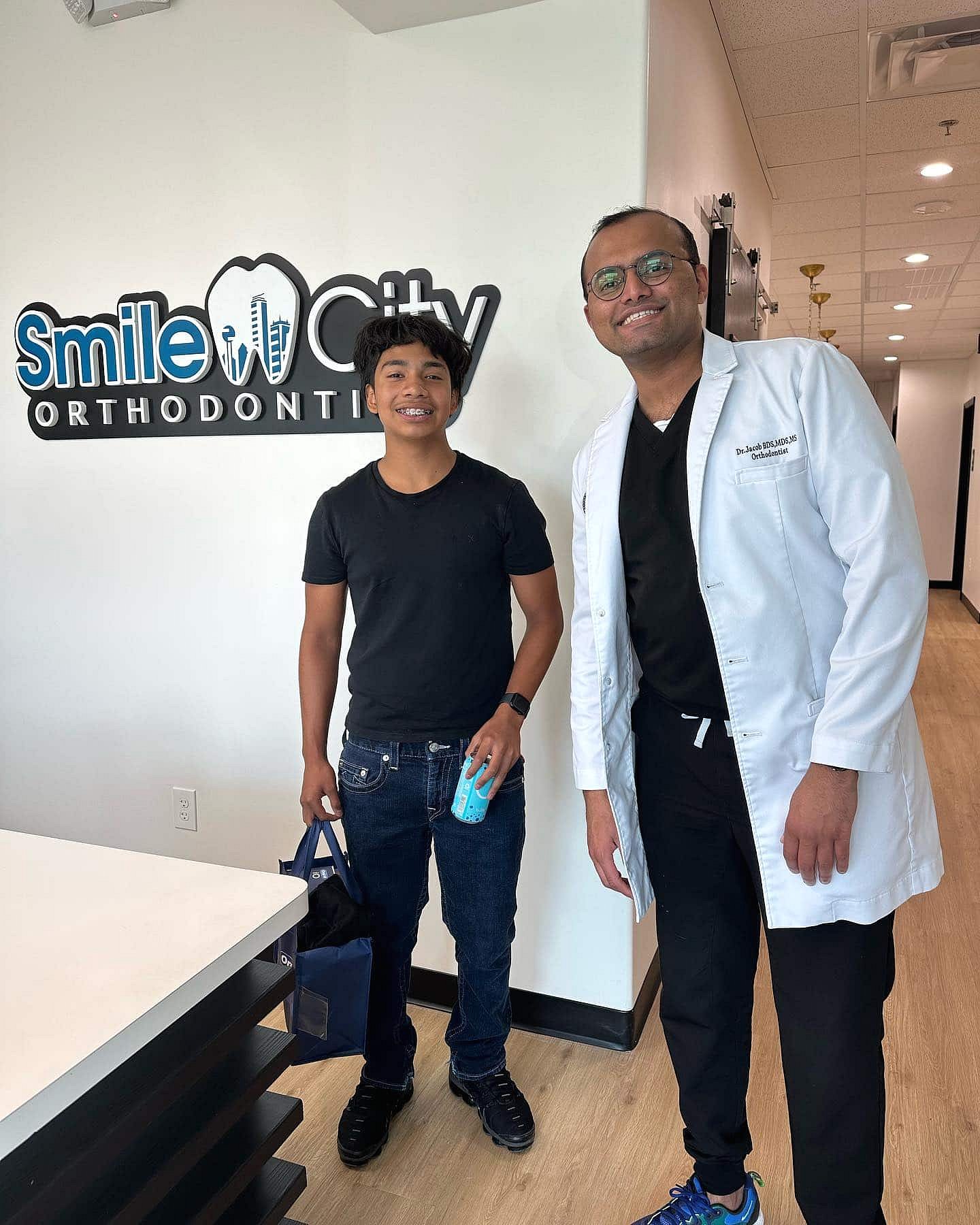 Inside the Smile City Orthodontics office in Sunnyvale, TX, a patient and an orthodontist in a white coat smile together for the camera.