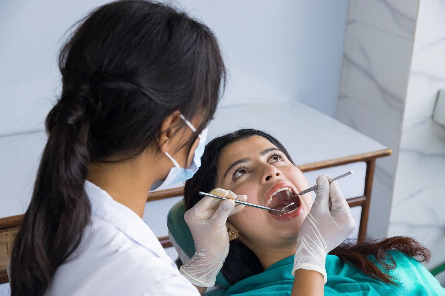 At Smile City Orthodontics in Mesquite TX, a dentist wearing gloves and a mask examines a woman's open mouth with dental instruments in the clinic.