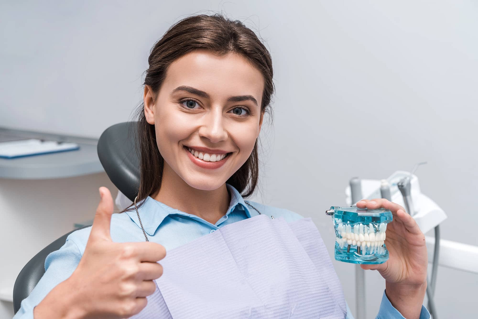 At Smile City Orthodontics in Mesquite TX, a woman in a dental chair smiles while holding a dental model and giving a thumbs-up, with dental equipment visible in the background.