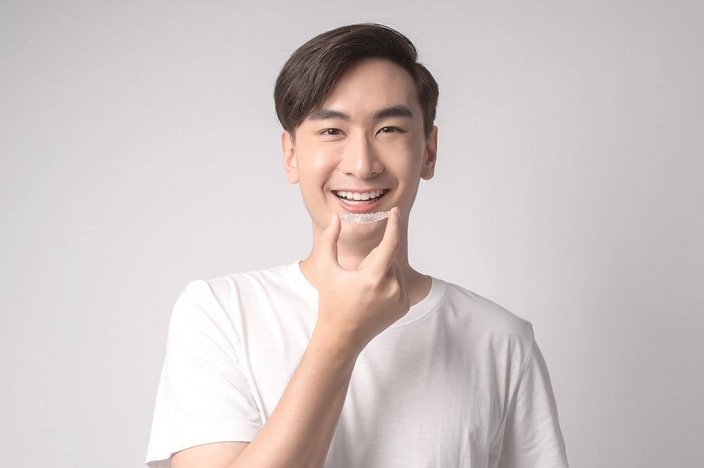 Smiling man pointing to teeth while holding Invisalign aligner – can Invisalign fix overbite in Sunnyvale, TX.
